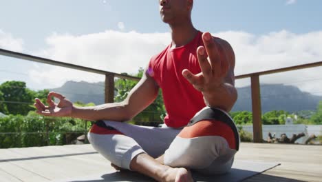 midsection of relaxed biracial man sitting on terrace and meditating