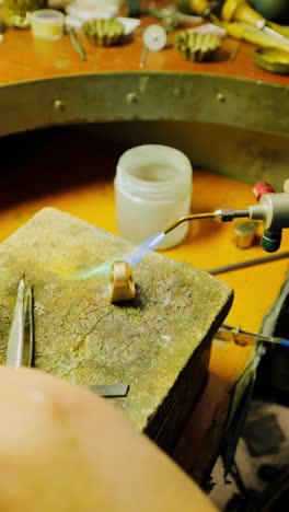 focused shot of artisan heating gold ring with blue flame in dim workshop light