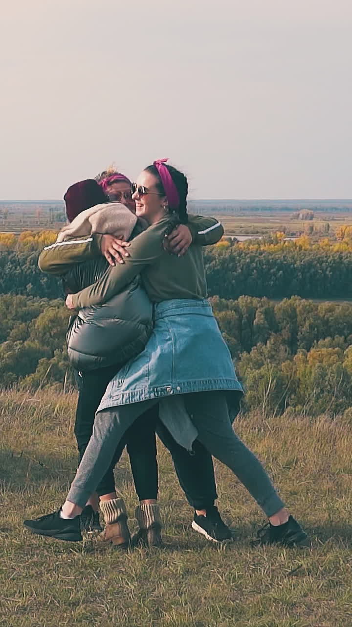 tipsy girls hug on meadow at blue tent against pictorial green and yellow autumn forests slow motion