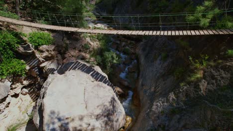 Hanging-wooden-walkway-over-a-mountain-stream-and-waterfall-with-colorful-turquoise-waters