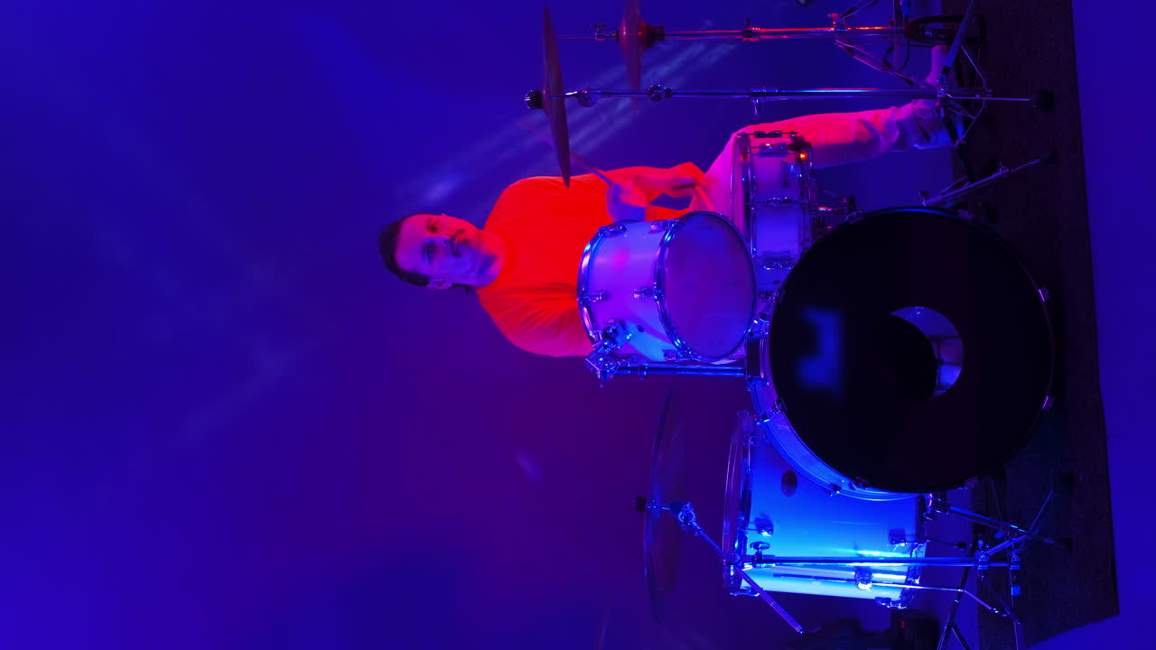 Cool grunge rock musician playing drums on stage doing an amazing metal solo lit by club neon red and blue lights.