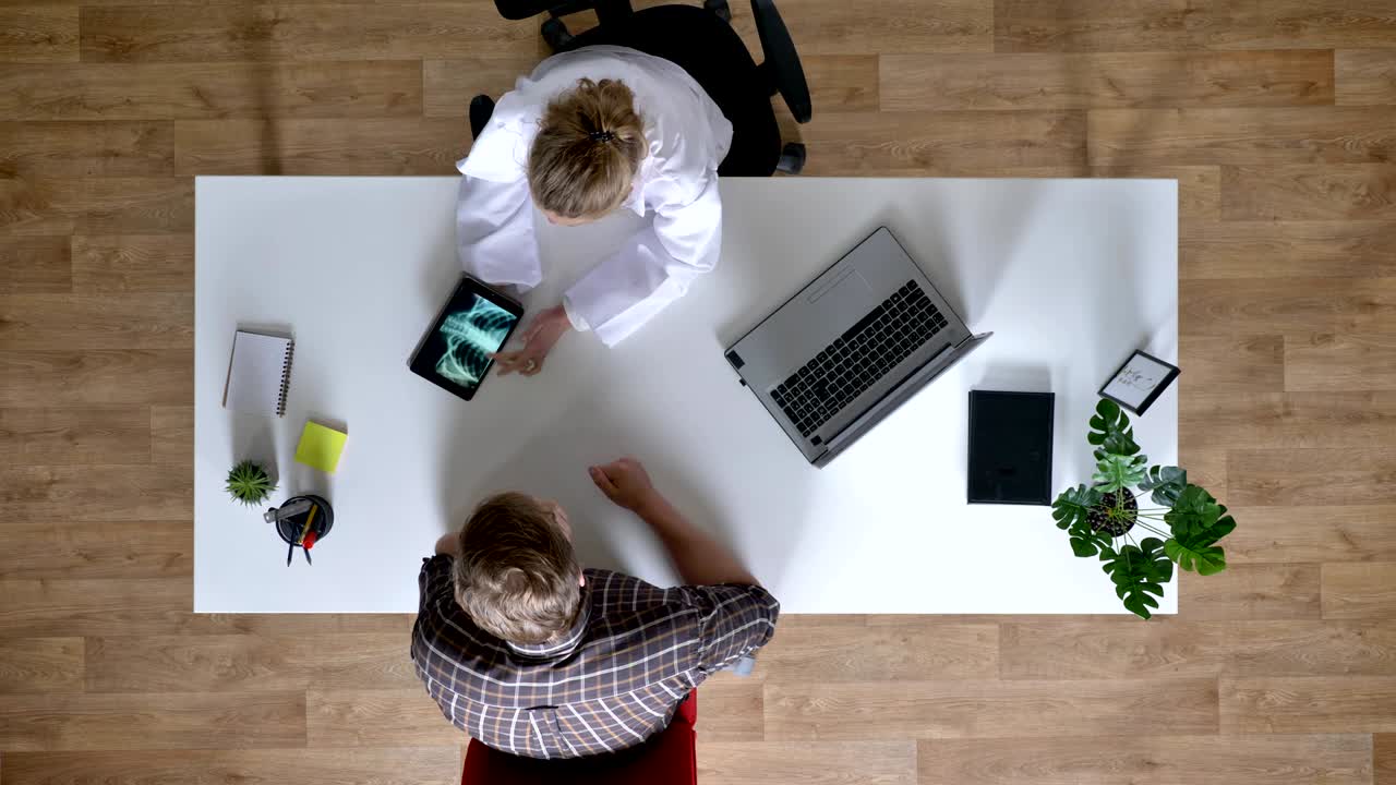 Ung kvindelig læge viser røntgenbillede på tablet til patienter og forklarer sygdom, mand hos lægen, medicinsk koncept, topbillede