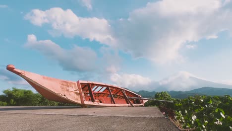 Wooden-Boat-Flips-On-Its-Side-At-The-Edge-Of-The-Seawall-With-The-Iconic-View-Of-Mayon-Volcano-Visible-From-Afar-In-Malilipot,-Albay,-Philippines---Timelapse