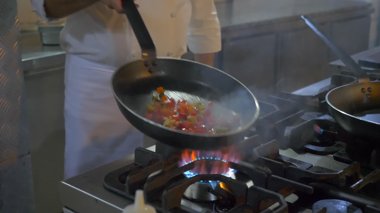 un chef en la cocina cocinando y mezclando pimientos con una gran llama, cierra
