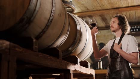 authentic shot of successful male sommelier is tasting a flavor and checking white wine quality poured in transparent glass in a wine cellar.