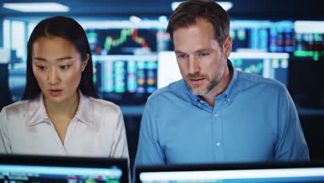 two professionals focus intently on financial charts and data in a tech-driven office environment. the atmosphere emphasizes teamwork and analytical skills, showcasing a dynamic work culture.