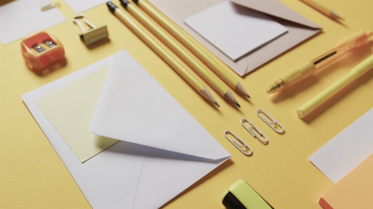 primer plano de bolígrafos, lápices y papelería dispuestos sobre un fondo amarillo, en cámara lenta