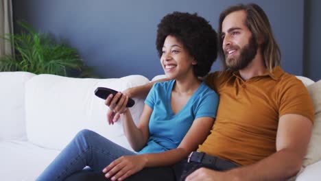 mixed race couple watching tv together while sitting on the couch at home