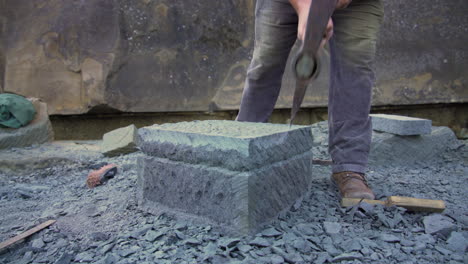 handheld shot of a local stone craftsman shaping stone pillar with a hand pick, in the city of ancud, chiloe island