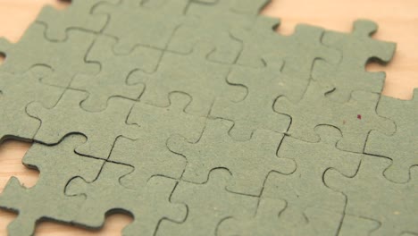 close up of a young girl's hand putting a puzzle piece in the last blank spot concluding a single color puzzle, on a light wooden background