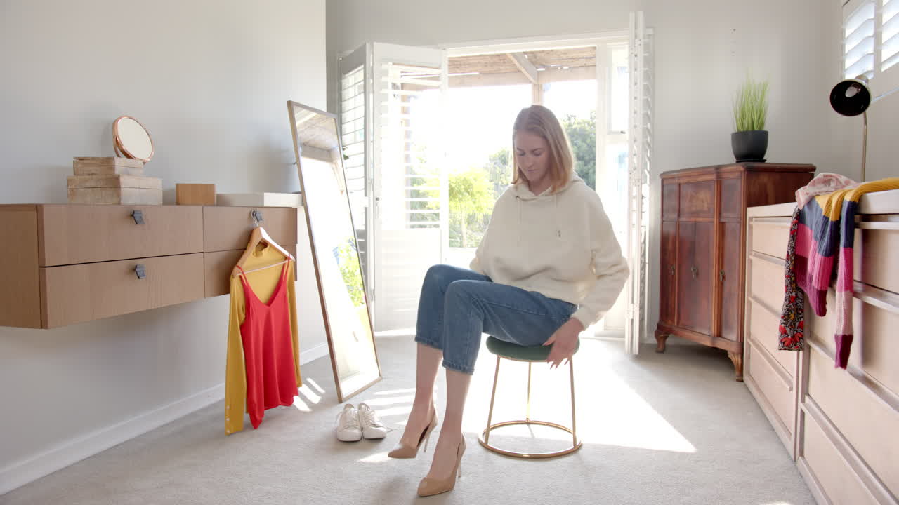 Woman arranging stool in bright bedroom with clothes and shoes around