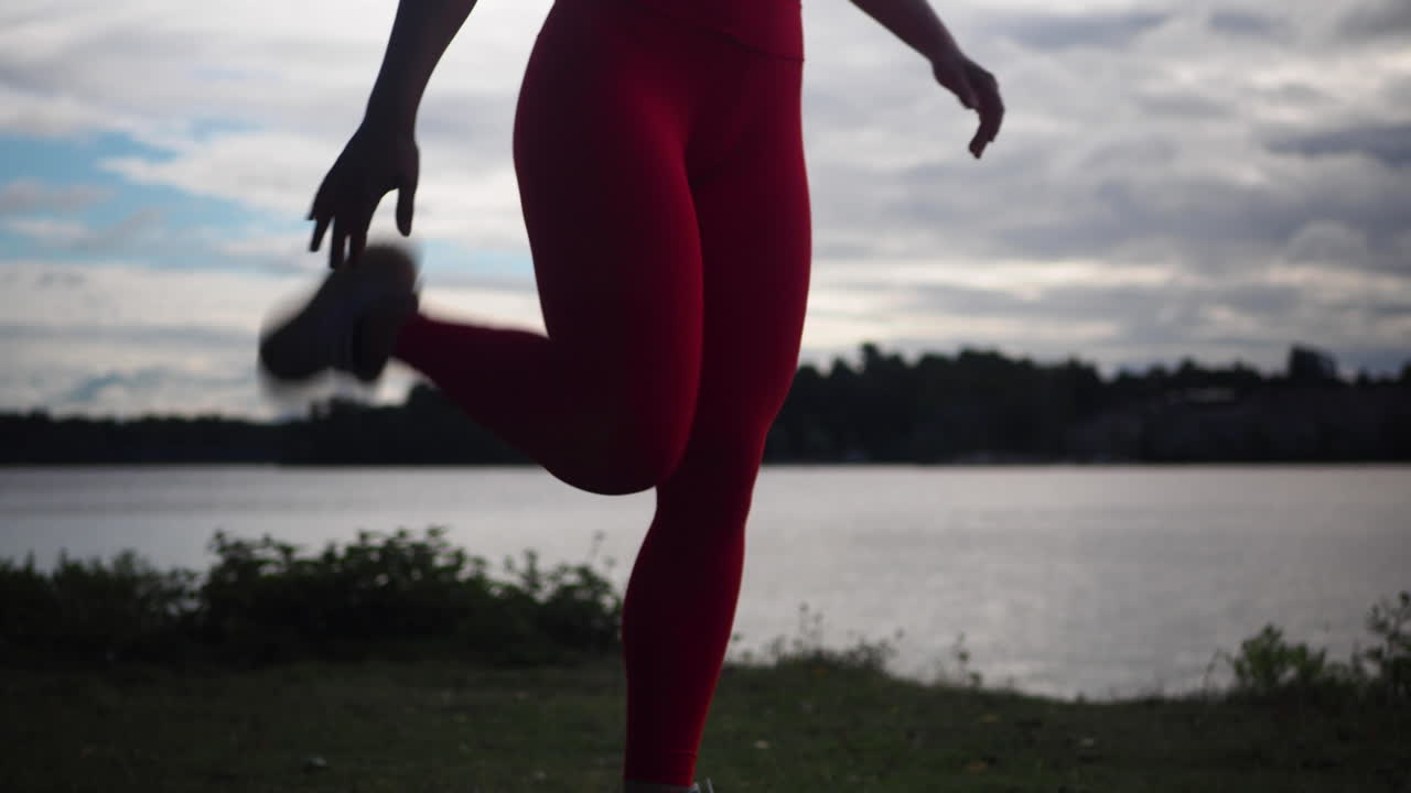 Jovem mulher de leggings vermelhas fazendo exercícios e praticando yoga ao ar livre perto do lago