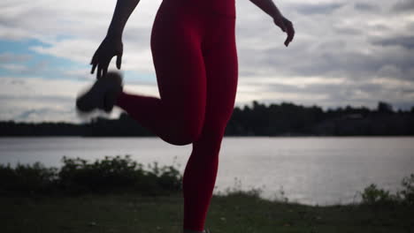 young woman in red leggings doing exercises and practicing yoga outside near lake