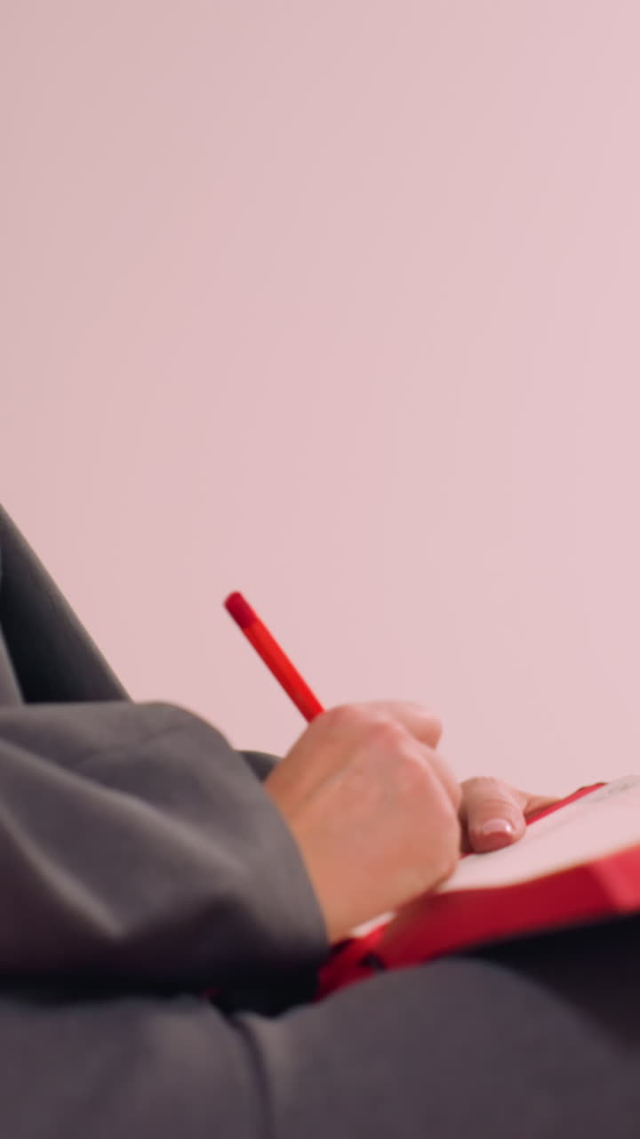 Professionista in abbigliamento da lavoro che tiene in mano una penna, guarda pensierosa di lato. Sembra immersa nei suoi pensieri mentre sistema la penna, vista di profilo laterale, ambientazione con sfondo neutro.
