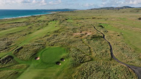 golf course drone flyover of rolling green fairways on ireland links golf course along coastline