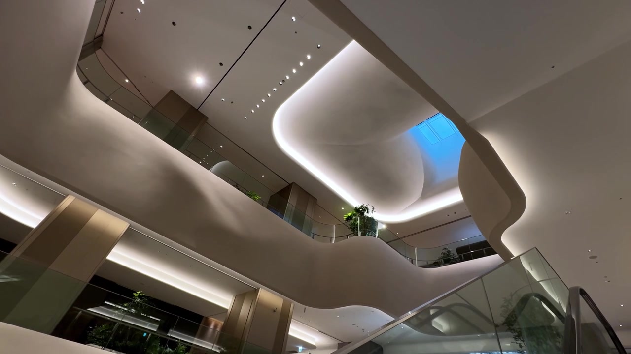 A sleek modern interior with curved architecture and escalators under soft ambient lighting