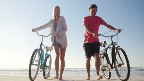 couple walking with bicycles at beach