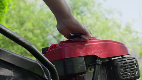 Hand-starting-a-red-lawn-mower-on-a-sunny-day-with-greenery