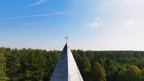 tomada de un dron de una remota torre de piedra de la iglesia y la cruz en el medio del bosque en la noche nublada en lituania