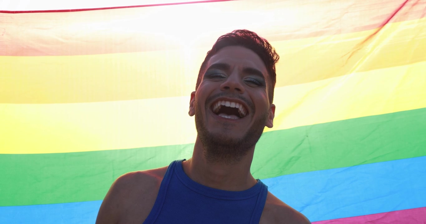 Homem Maquiado Rindo com a Bandeira do Orgulho LGBTQIA+