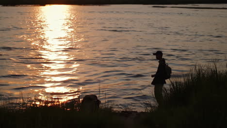 silhouette of person by a river at sunset