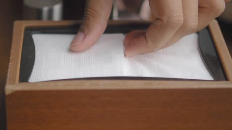 close up of a hand pulling a napkin from a wooden box