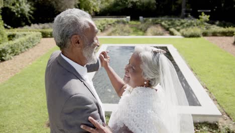 feliz pareja biracial senior caminando, bailando en la boda en el jardín, cámara lenta