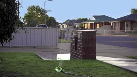 un aspersor riega el césped delantero de una casa suburbana