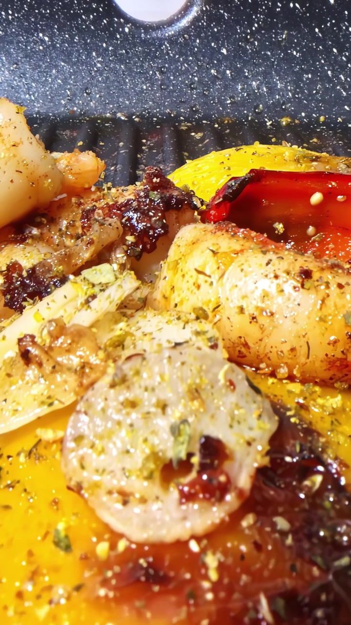 Golden cooked shrimp and roasted red yellow peppers with green dry seasoning and golden juices on ridged grill pan ready to plate, dolly in vertical video