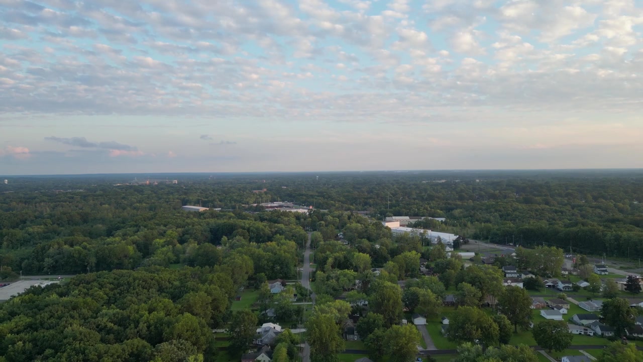 Aerial view of a vast, tree-covered suburban area under a sky dotted with soft clouds. Ideal for content about suburban living, nature in urban spaces, and landscape photography.