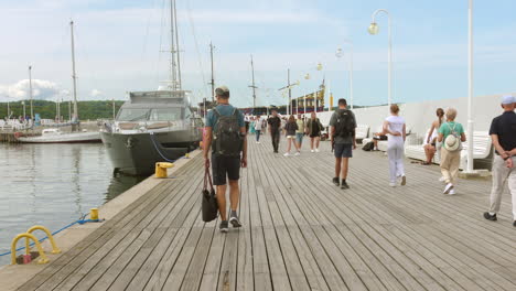 people walking on a wooden pier with boats and a yacht