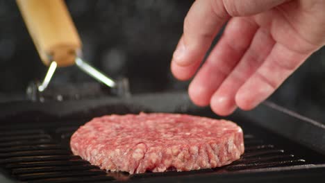 la mano de los hombres pone la carne cruda de la hamburguesa en una sartén para cocinarla.