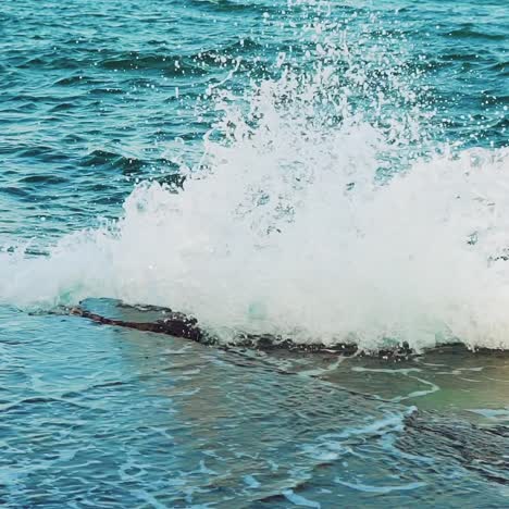 turquoise waves is colliding with stone rocks near the shore and turning into thousands of drops of water. slow motion. view from above