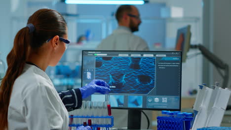 científico médico mirando una muestra de sangre y escribiendo en la computadora