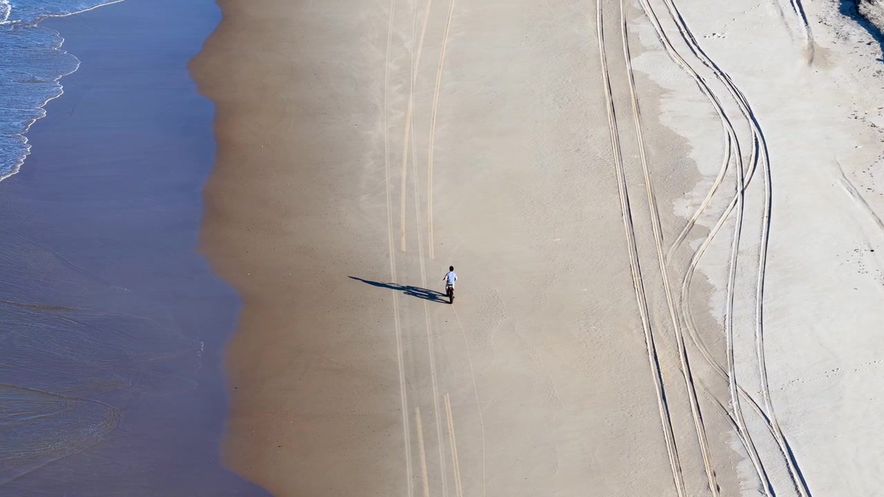 High angle aerial shot of a cyclist riding along the shoreline at South Stradbroke Island.
