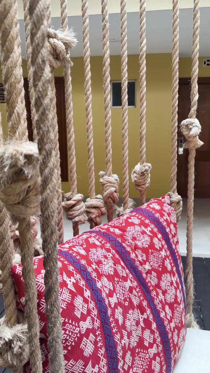Divisorio in macramè di corda fatto a mano con cuscino fantasia in un ambiente interno accogliente.