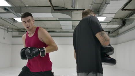 Two-men-in-a-white-gym.-The-coach-and-the-fighter-work-out-the-kick-in-the-jump-knee-on-the-paws-in-slow-motion