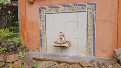 vista de seguimiento de una pequeña fuente de azulejos con escultura femenina y paredes de roca con plantas