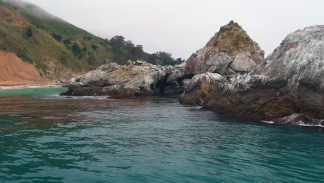 coastal boulders stick out pacific ocean in big sur on a calm day, low aerial