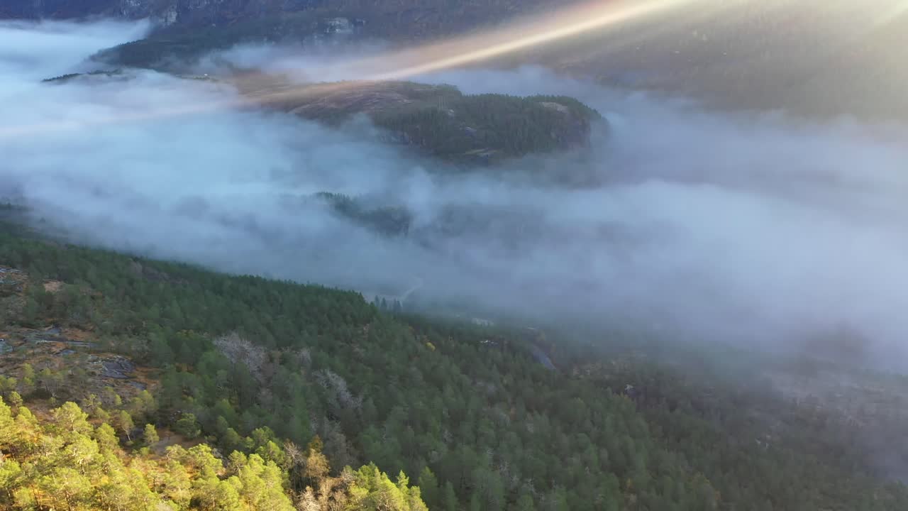 neblina matutina llenando el fondo del valle de eksingedalen mientras los primeros rayos de sol penetran a través del marco superior - antena en movimiento descendente hacia la carretera en el fondo del valle - noruega