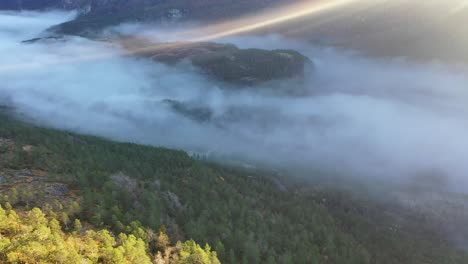 morning haze filling bottom of eksingedalen valley while first sun rays penetrating through top frame- downward moving aerial towards road in bottom of valley - norway