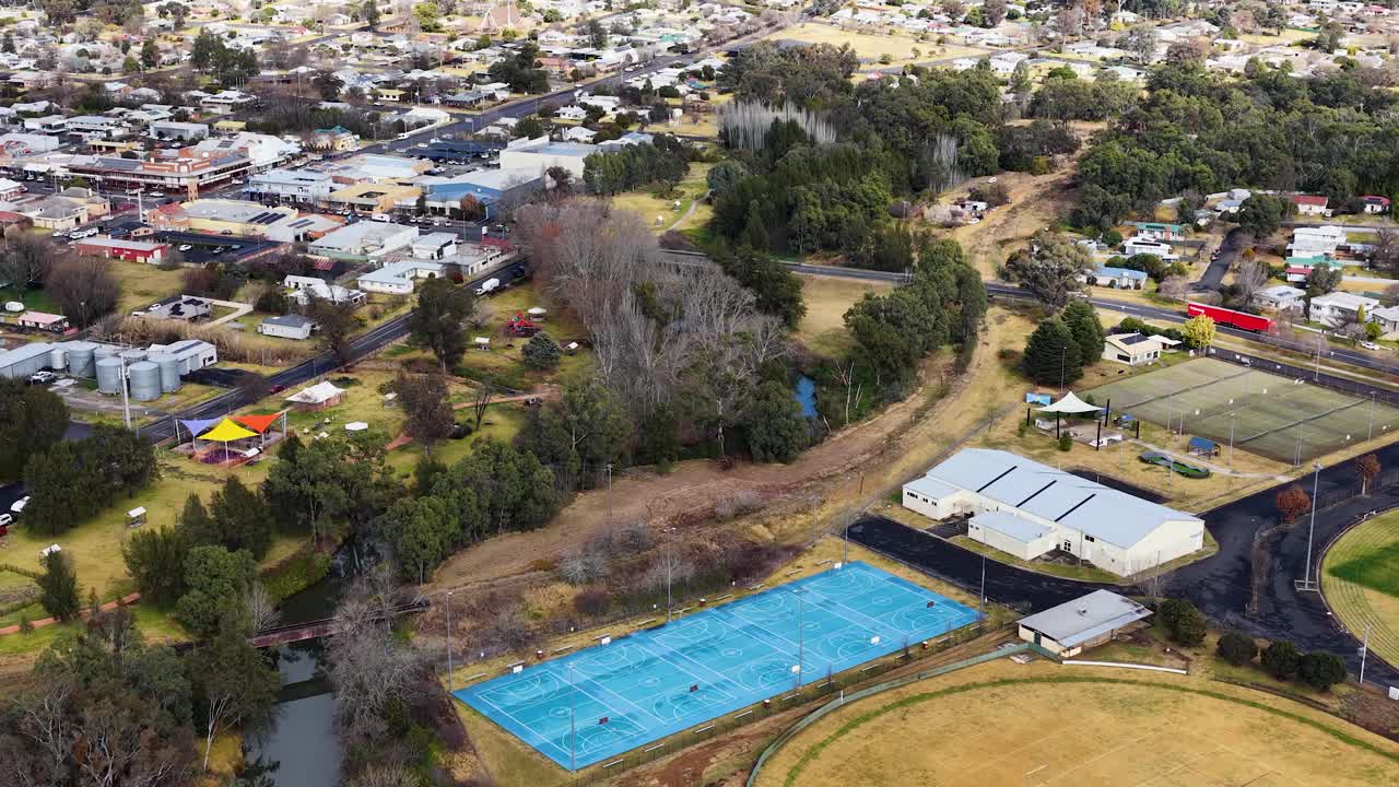 Drone footage glides above sports fields, tennis courts, and residential streets in Coonabarabran, NSW, under soft daylight with steady, smooth camera movement