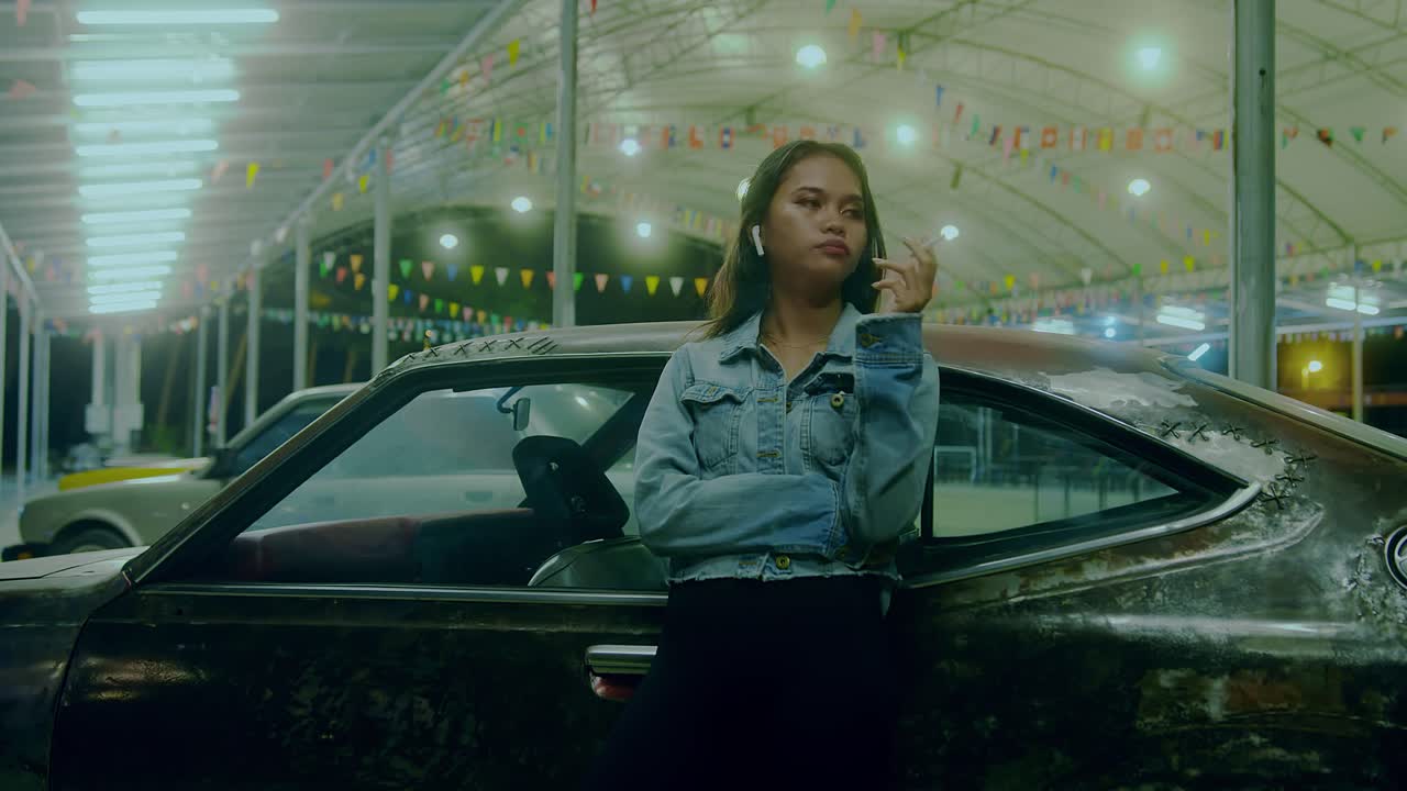 Woman with Earbuds Leaning on Vintage Rusty Car at Night