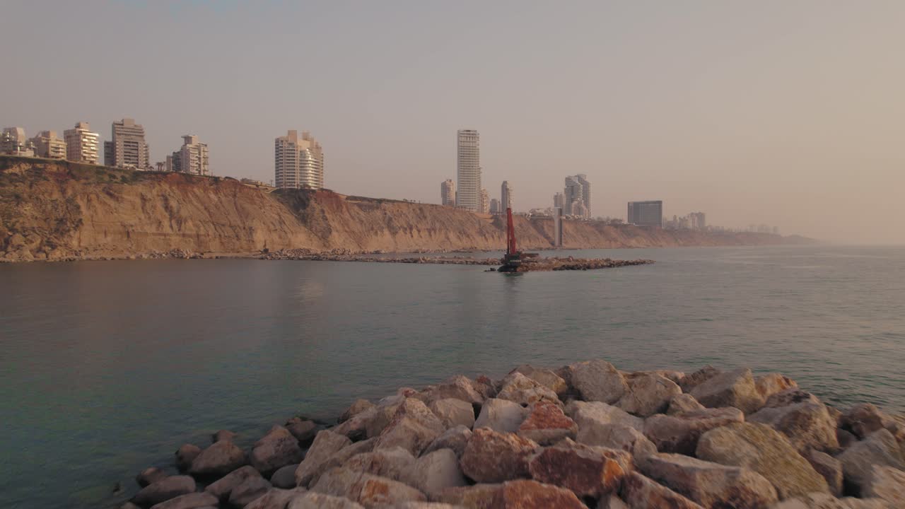 empuje al atardecer a una sola máquina excavadora que construye un muelle de piedra en el mar