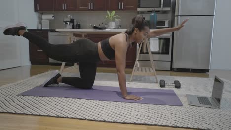 a static shot of a black female doing poses in front of her lap top computer on her kitchen floor in her home