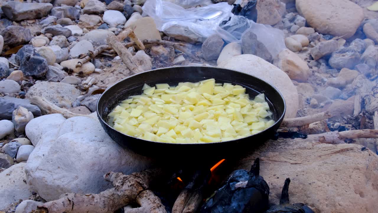 papas picadas hirviendo y cocinando en una fogata abierta en un ambiente natural al aire libre, preparando el almuerzo en llamas durante una caminata