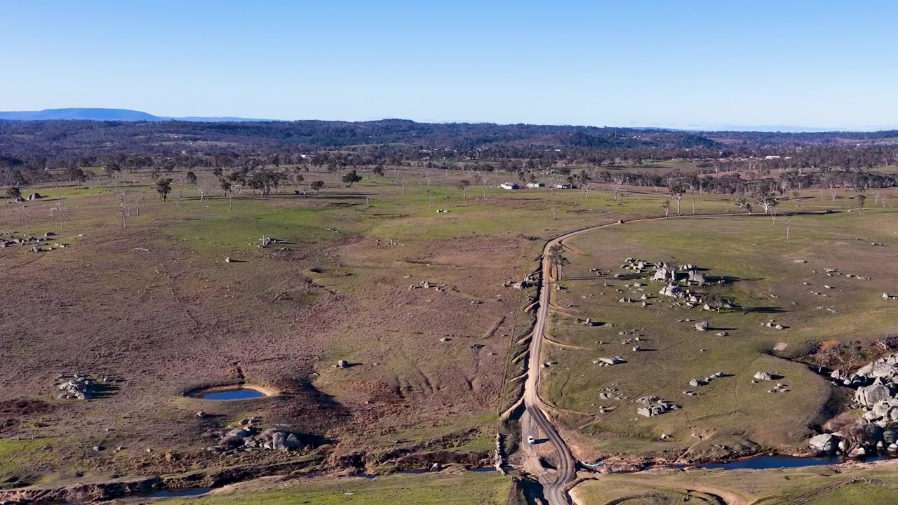 Ripresa aerea con drone dall'alto di una strada sterrata sinuosa attraverso un terreno roccioso dell'outback a Uralla, Australia