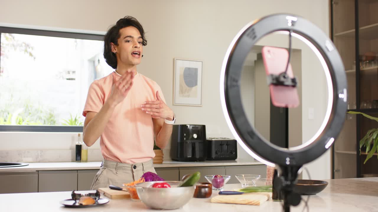 Male cook greeting audience, showing ingredients on kitchen island and explaining steps for recipe