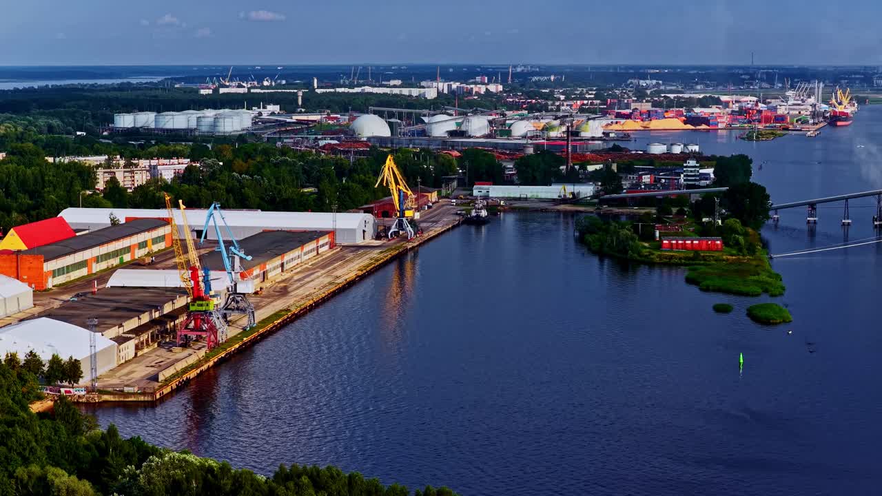 Aerial establishing of industrial waterfront with red-roofed buildings and boats, cranes loading natural resource minerals
