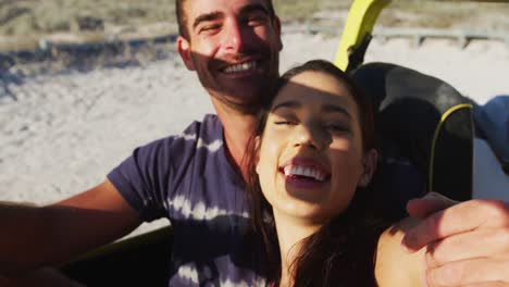 Feliz-Pareja-Caucásica-Sentada-En-Un-Buggy-De-Playa-Junto-Al-Mar-Usando-Un-Teléfono-Inteligente-Tomando-Selfies